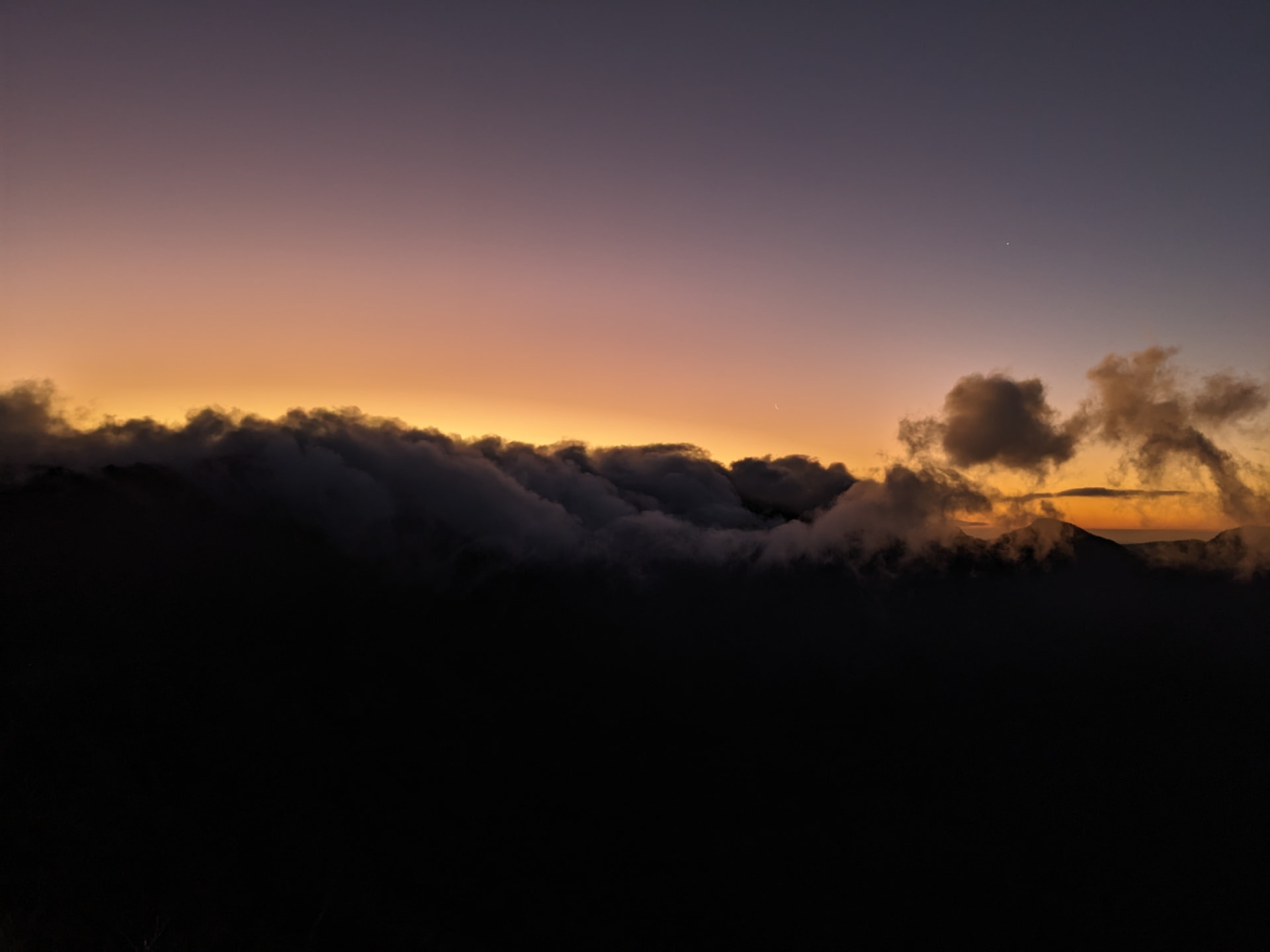 A sea of clouds rolling over dark mountains at dusk